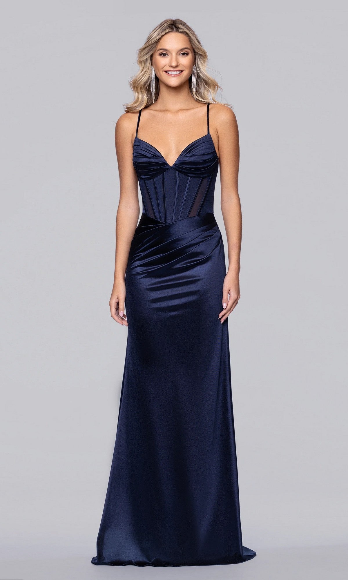 A woman wears the Blondie Nites 6014BN long navy prom dress with spaghetti straps and a fitted corset bodice, standing against a plain light gray background.